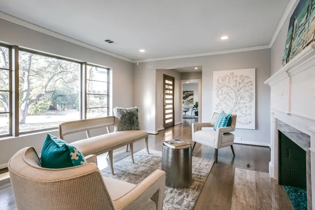Living room with large black-framed windows, a cream bench and a teal-accented chair looking toward the entry.