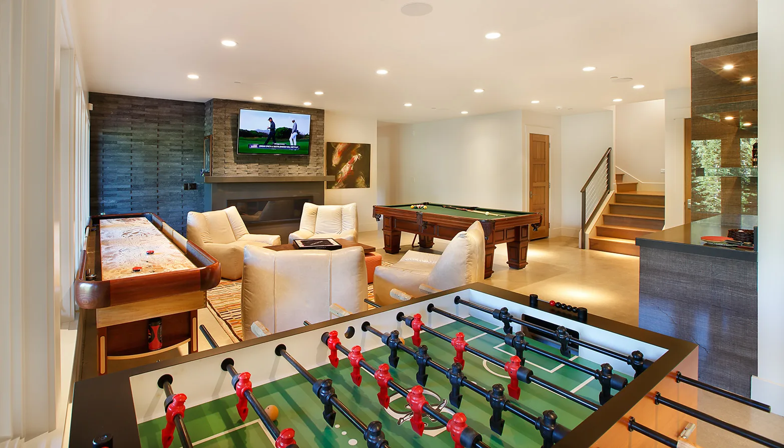 Game room with a foosball table and a staircase, open to a kitchen counter beyond