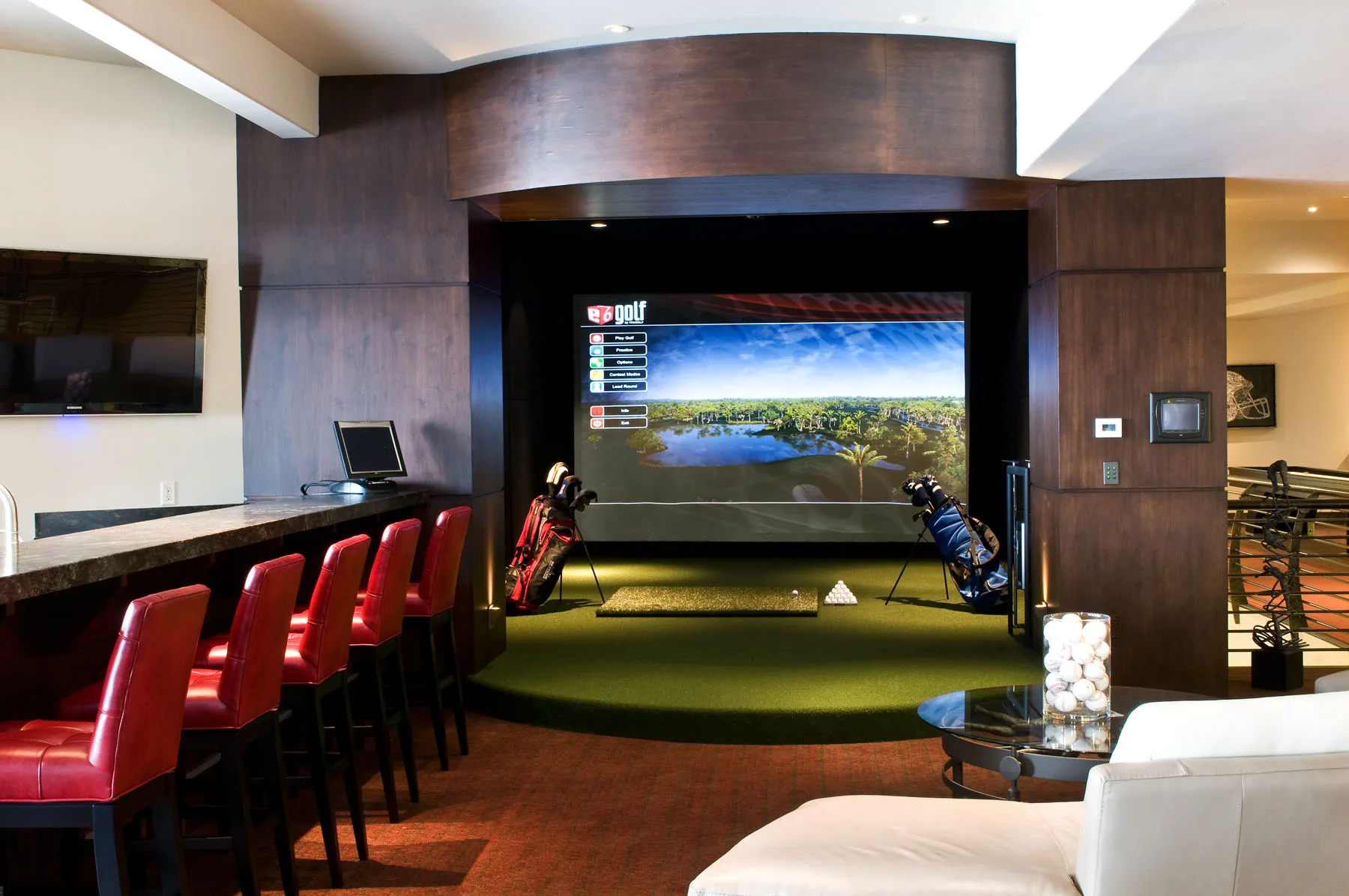 Golf simulator room with a projection screen, turf flooring and golf bags along the wall