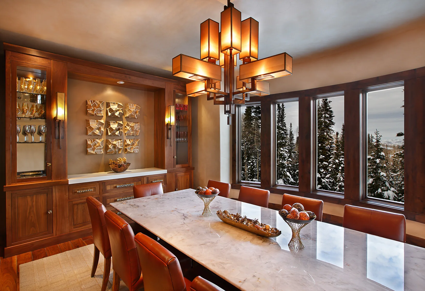 Dining room with a row of drum pendant lights over a long table, wood beam ceiling and windows looking onto trees
