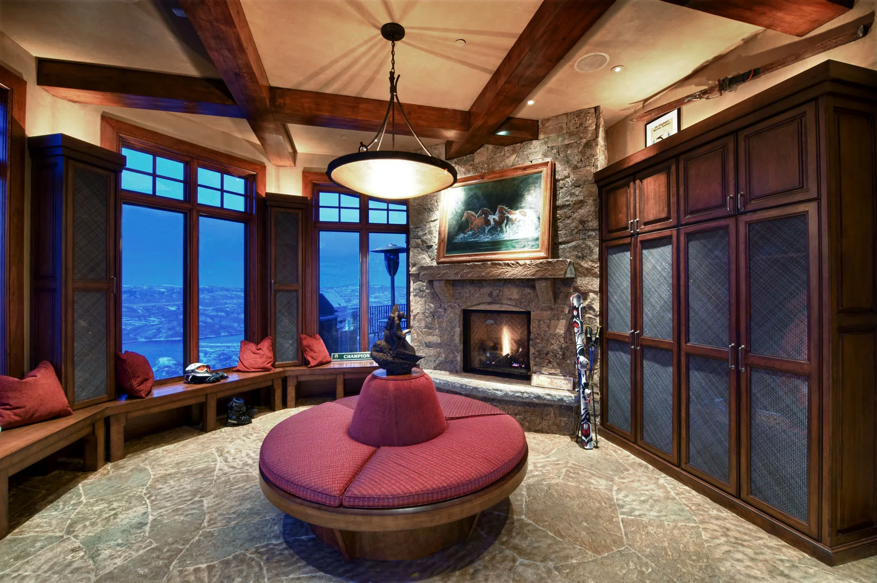 Sitting nook with a round red upholstered ottoman bench beside a stone fireplace and windows