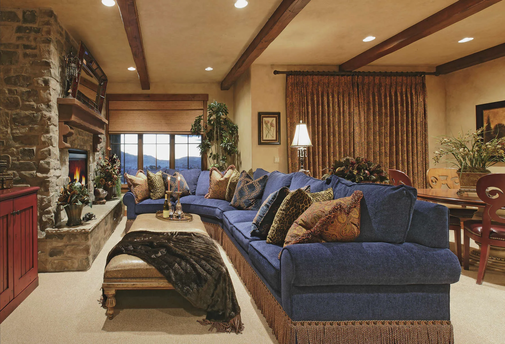 Living room with a blue sectional sofa, stone fireplace and wood beam ceiling