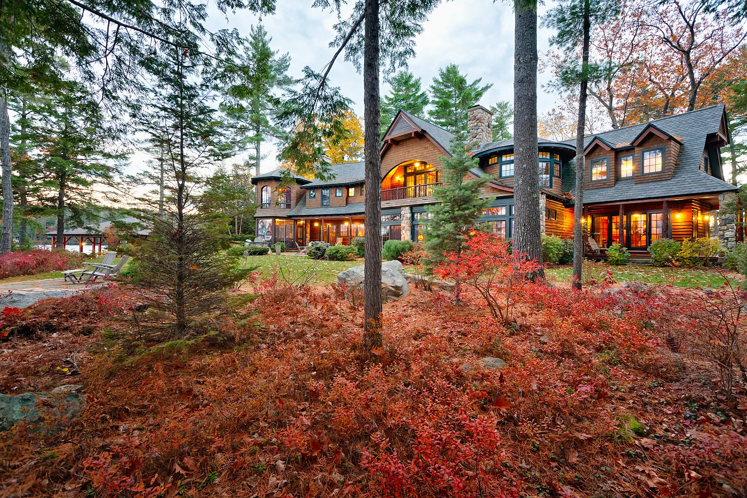 Shingle-style lake house exterior surrounded by red and orange fall foliage landscaping