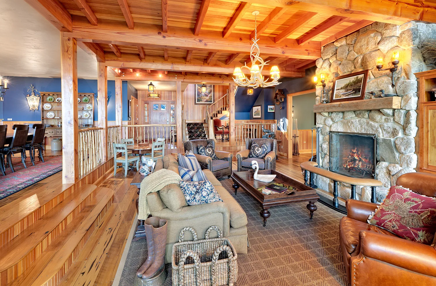 Great room with heavy timber trusses, a stone fireplace and an antler chandelier