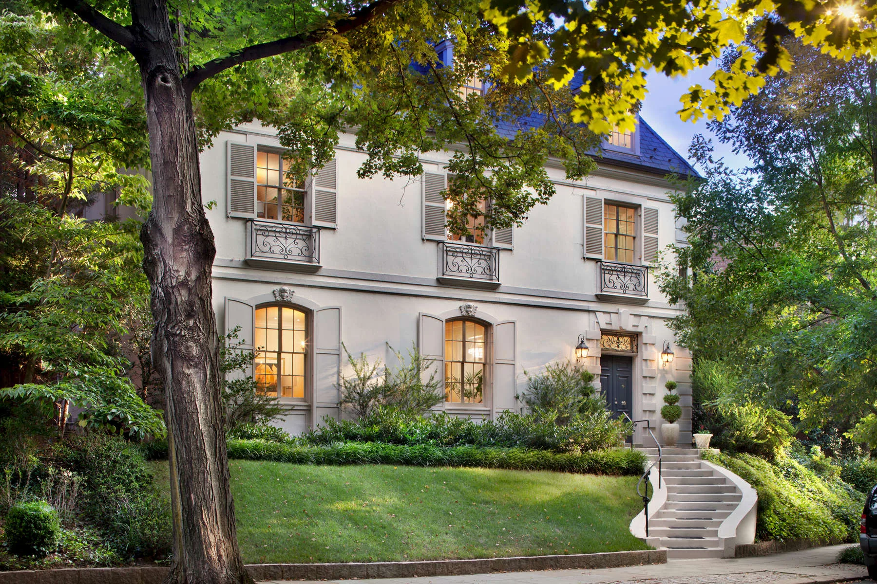 Dusk exterior of an elegant stone and stucco city home with manicured landscaping and lit windows