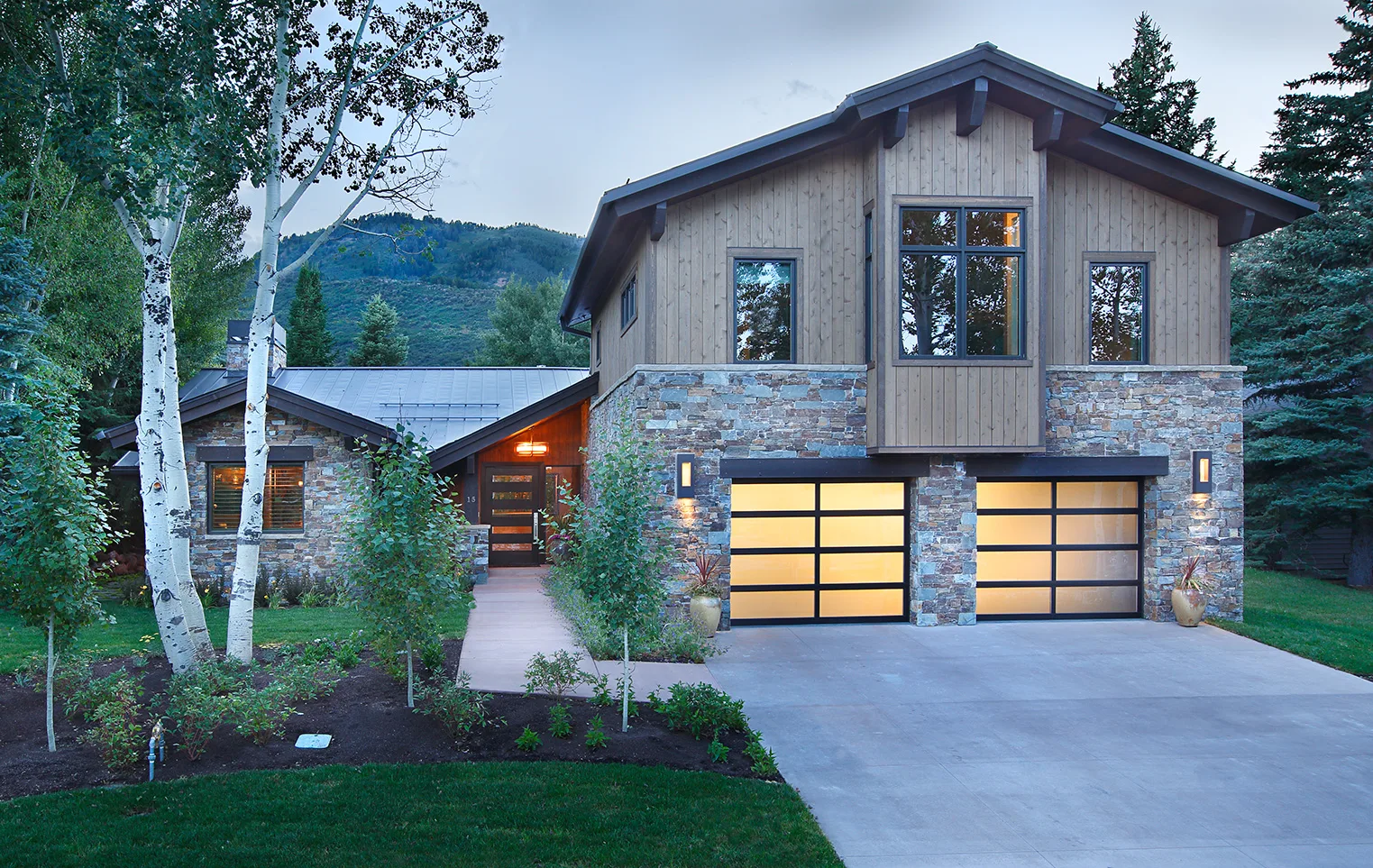 Daytime exterior of a stone and wood mountain home with a glass garage door and paved driveway
