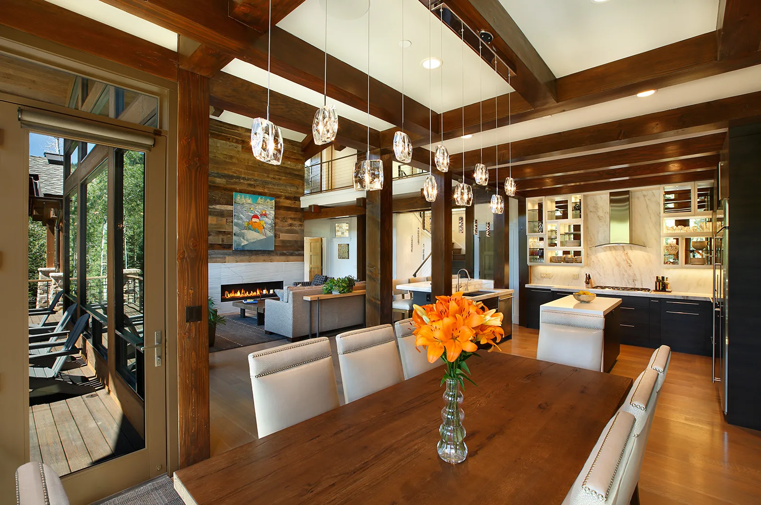 Dining area with a cluster of glass pendant lights over a wood table set with orange flowers, under a wood beam ceiling