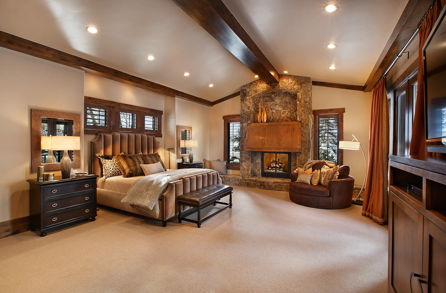 Bedroom with a wood headboard, beamed ceiling, fireplace and bedside table lamps
