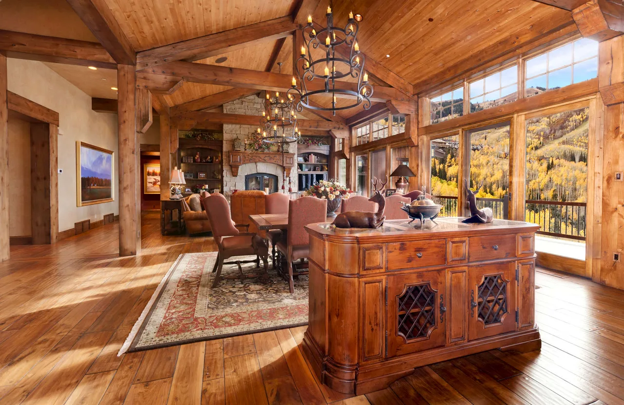 Great room with a wood buffet table, floor-to-ceiling windows showing fall foliage and an open timber ceiling