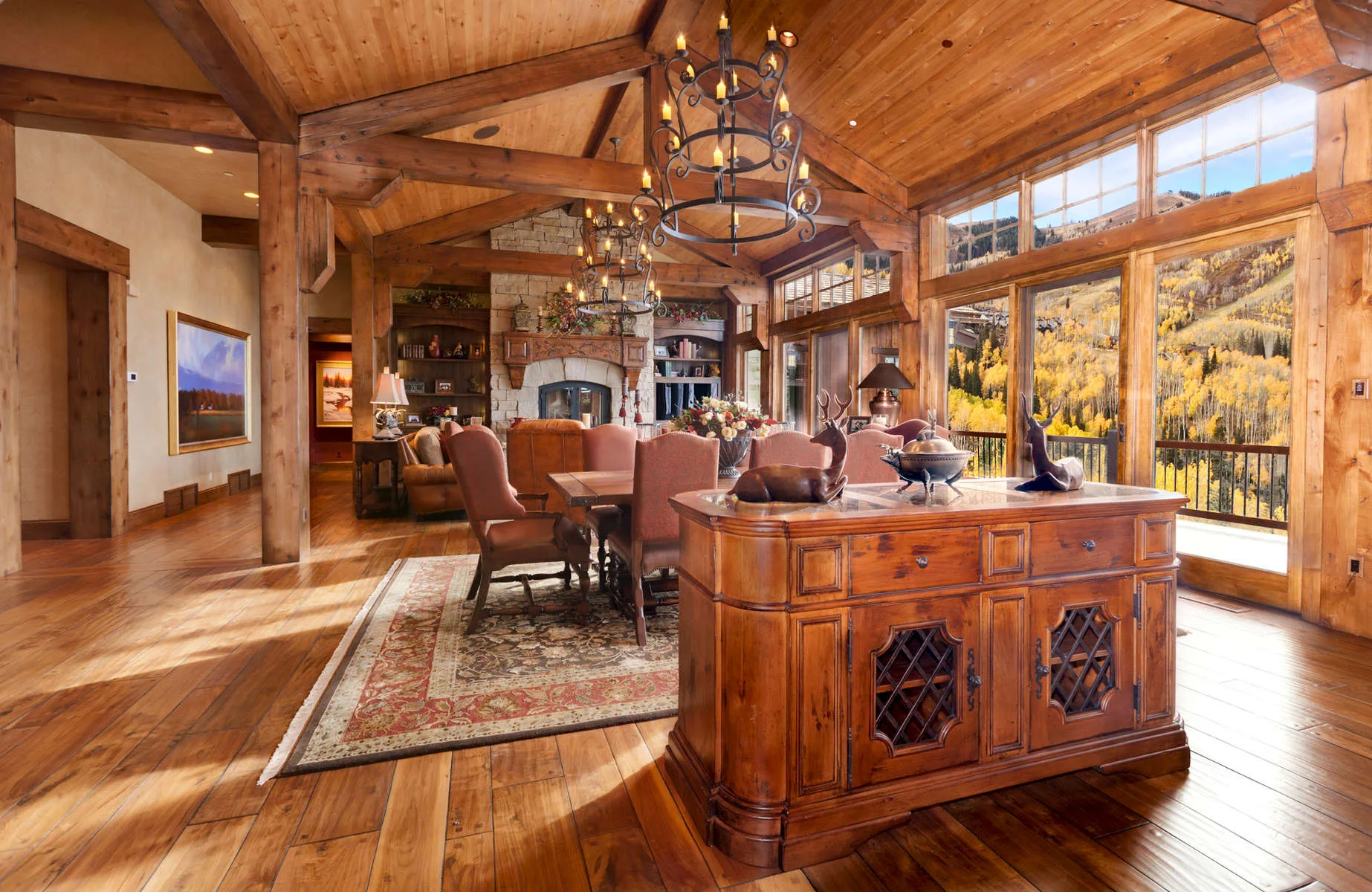 Great room with a wood buffet table, floor-to-ceiling windows showing fall foliage and an open timber ceiling