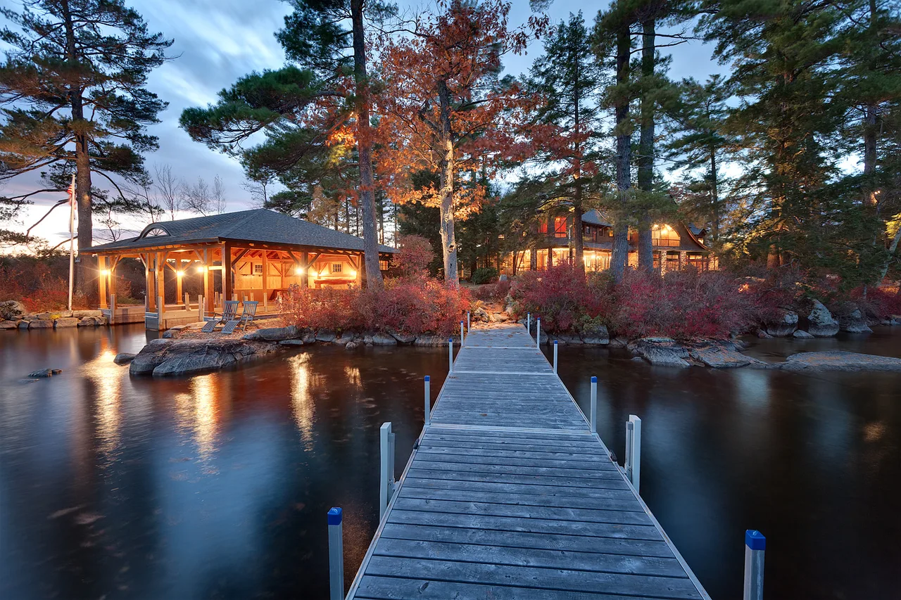 Dusk exterior of a lakeside home with a lit wooden boardwalk reflecting in the still water