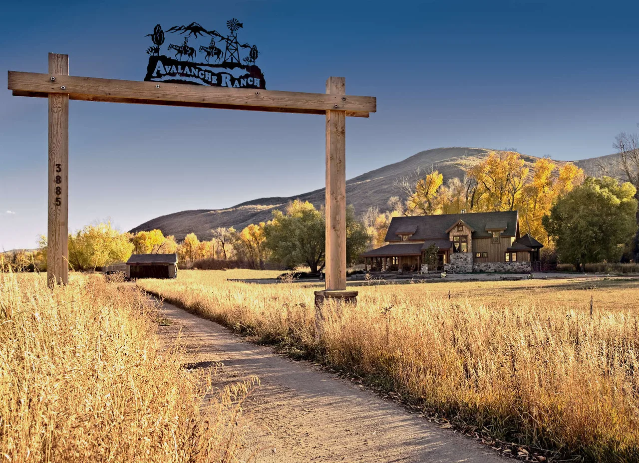 Carved wood entrance sign on a post with a mountain field backdrop