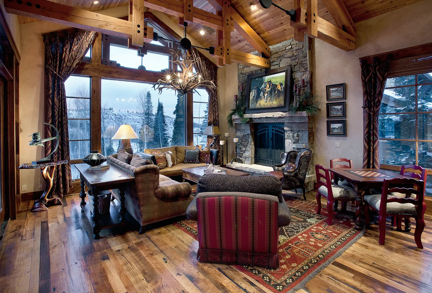 Living room with wood plank floors, timber beams, an antler chandelier and windows showing a mountain view