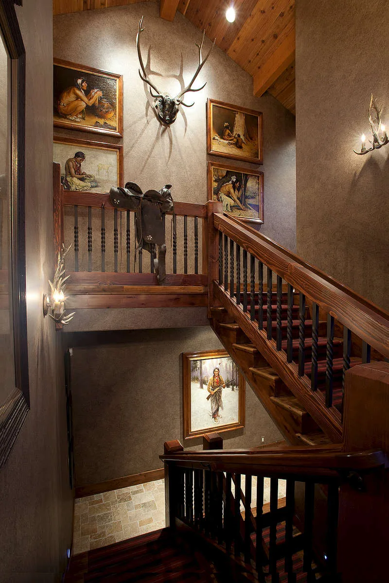 Stairwell with antler mounts and framed art on the wall beside a wood railing
