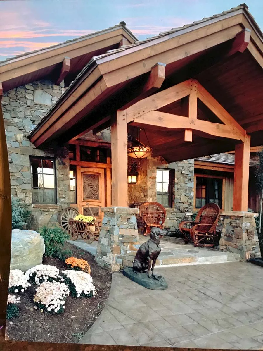 Covered stone-columned patio with wicker furniture and a dog statue in the garden beyond