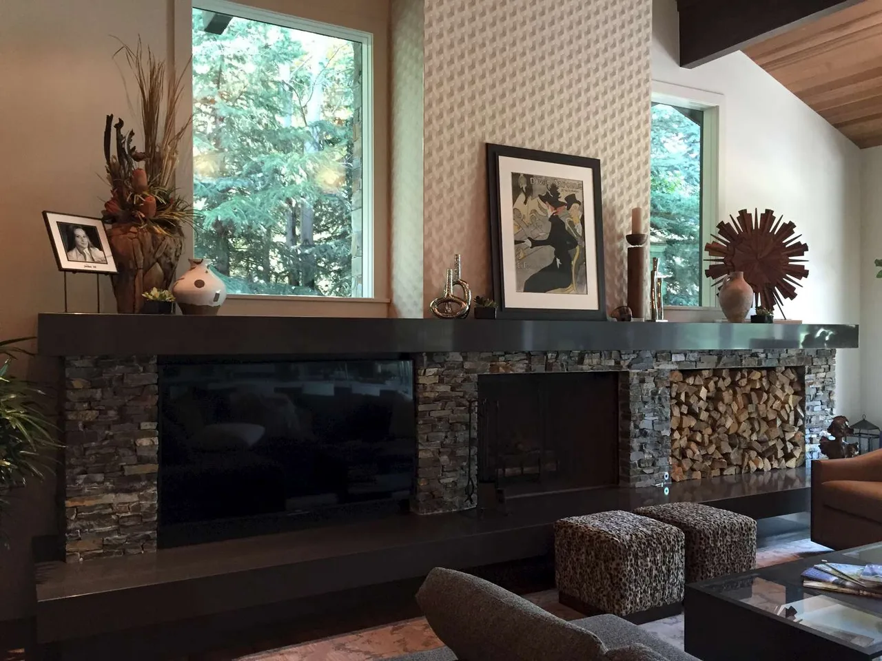 Living room with a stone fireplace, wood paneling and patterned curtains