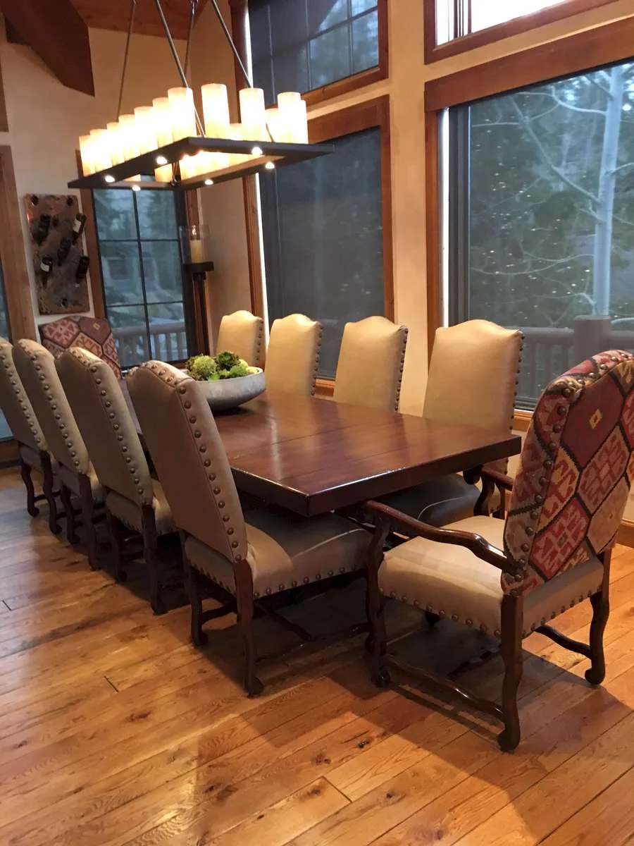 Dining room with a custom wood table, patterned upholstered chairs and a modern chandelier beside large windows