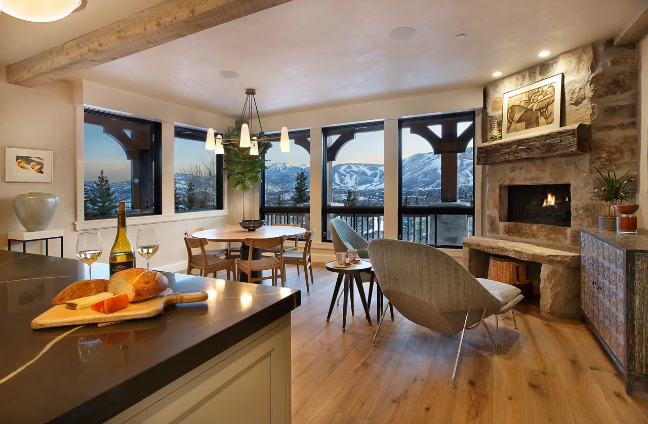 Dining nook by a wall of windows with a round table set with wine and cheese, a drum chandelier overhead and mountain views beyond