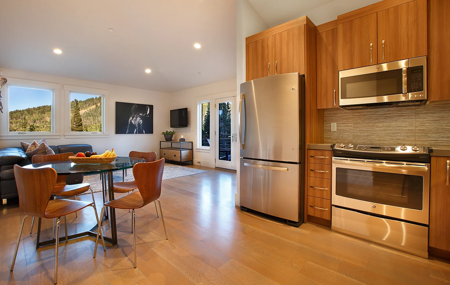 Breakfast nook with a round table and orange chairs beside a stainless refrigerator and wood floors