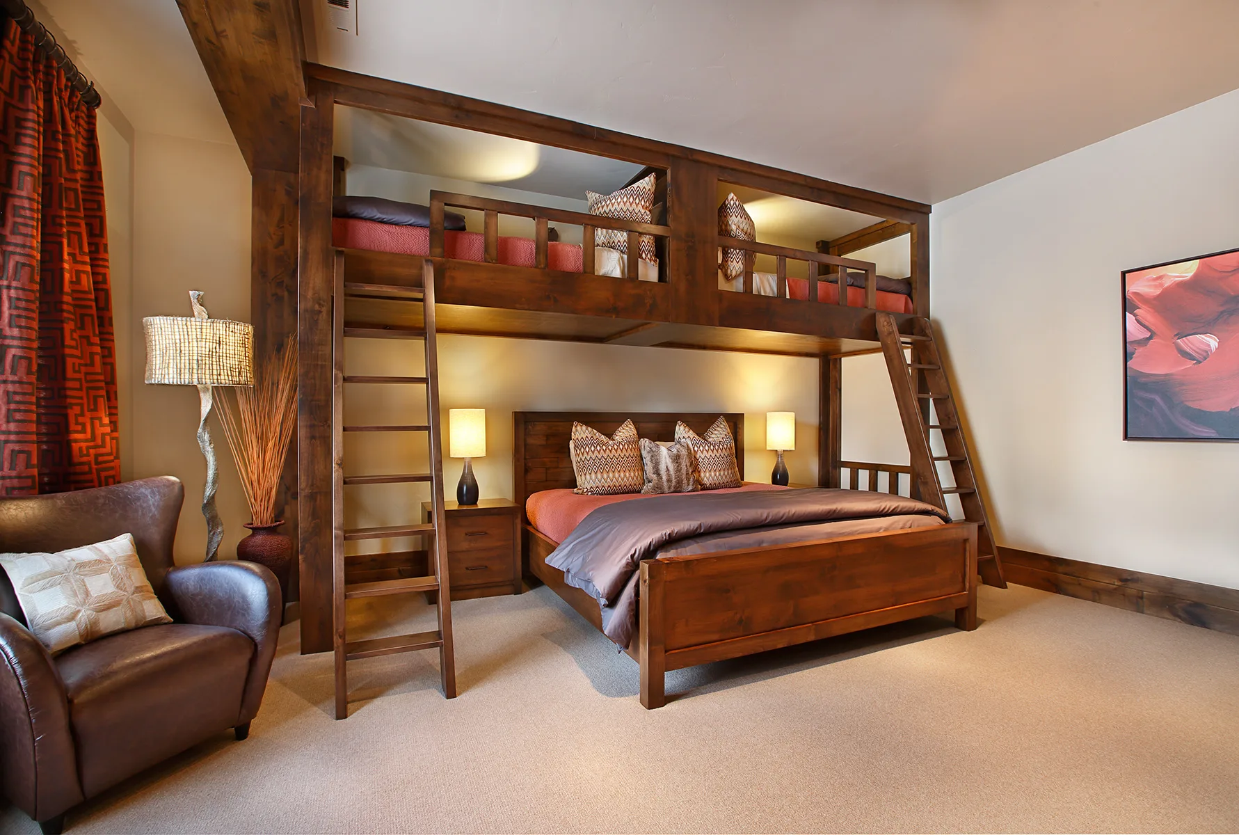 Bunk room with built-in bunk beds in red and orange bedding and a colorful painting on the wall