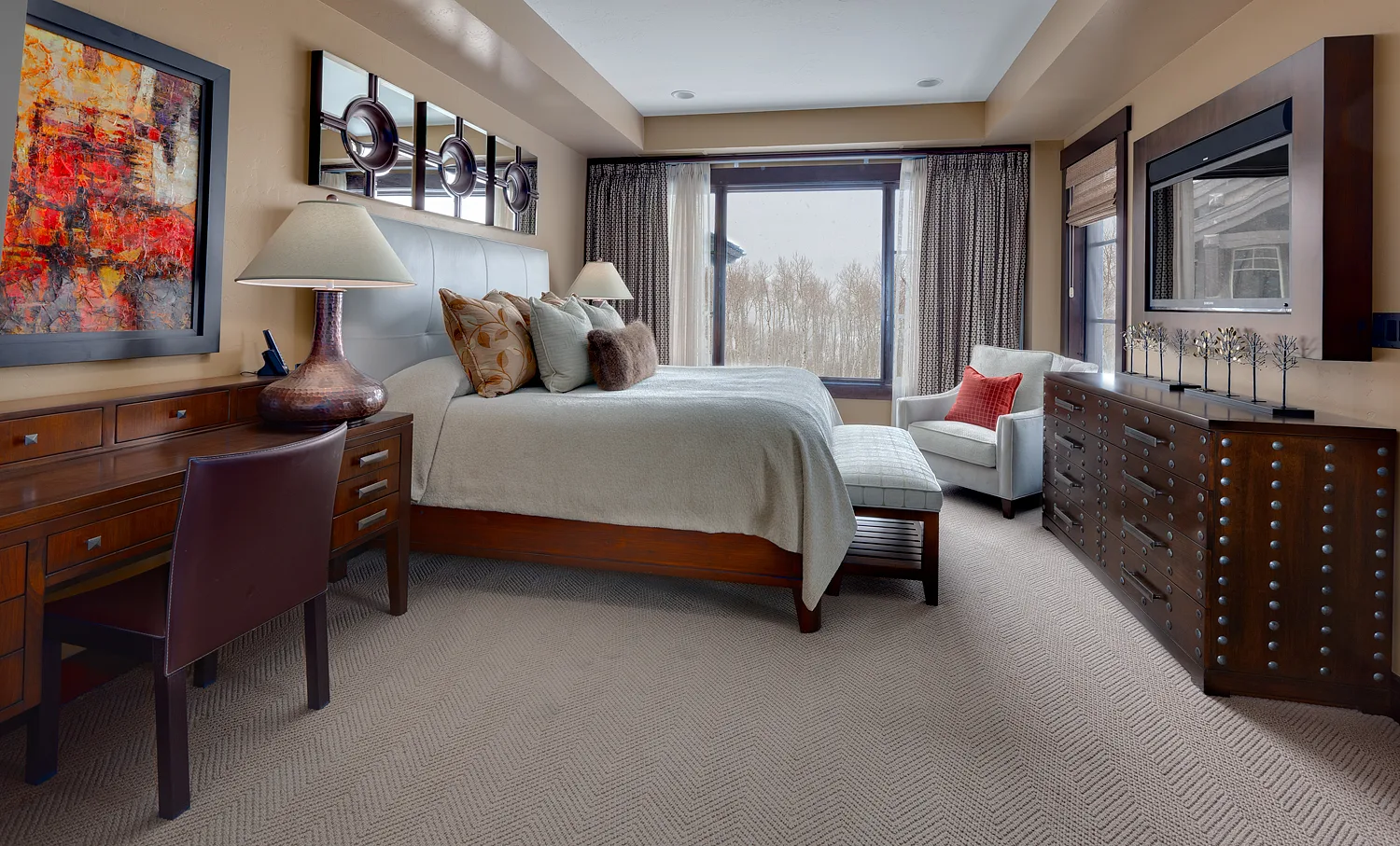 Bedroom with gray and white bedding, a chaise lounge and a large window with a mountain view beyond