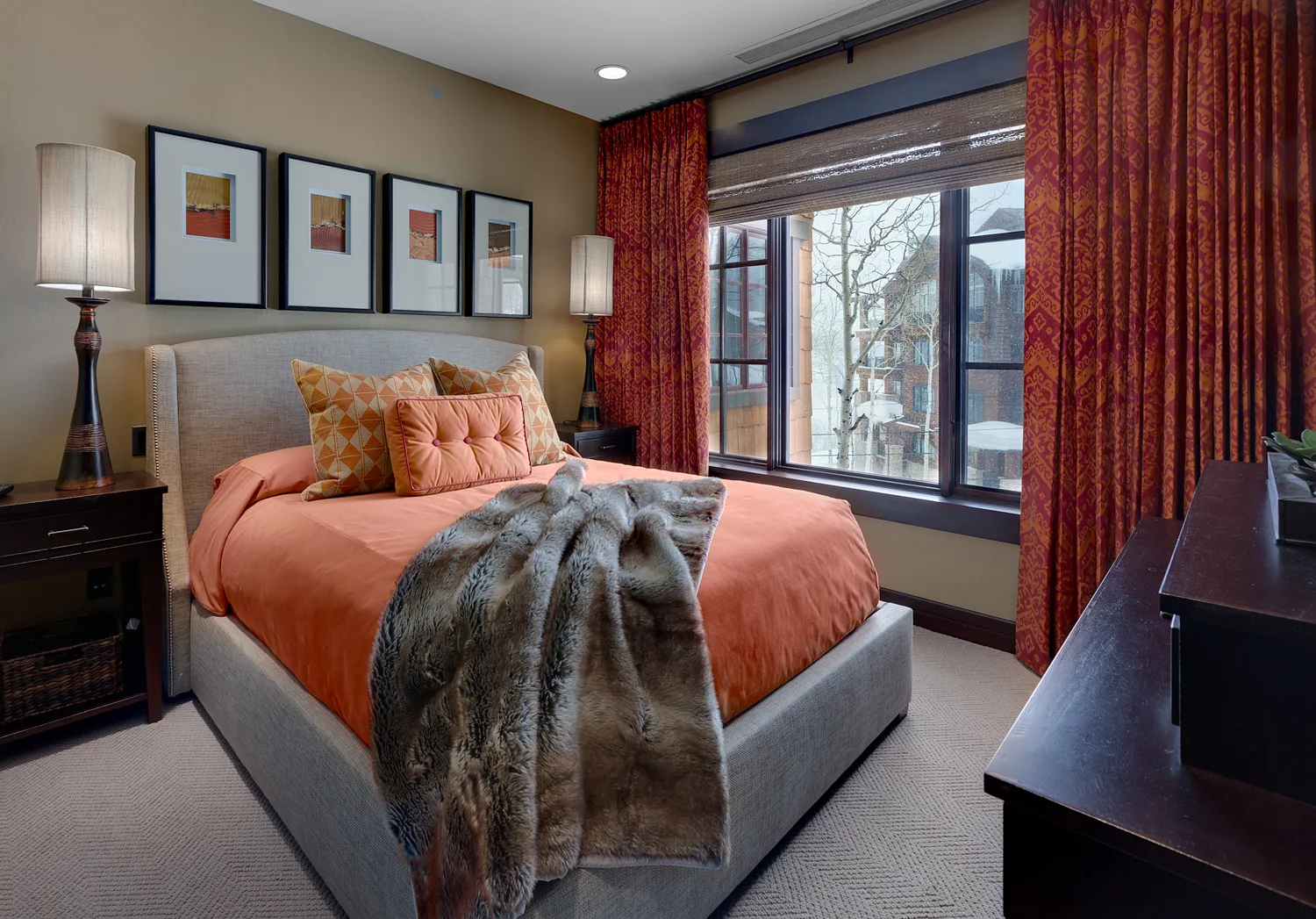 Bedroom with terracotta-orange bedding, red drapes and dark wood furniture