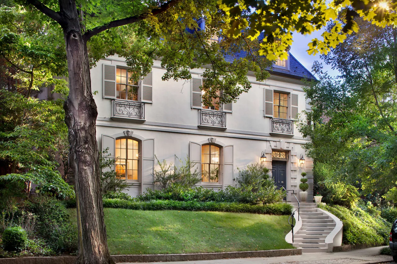 Dusk exterior of an elegant stone and stucco city home with manicured landscaping and lit windows