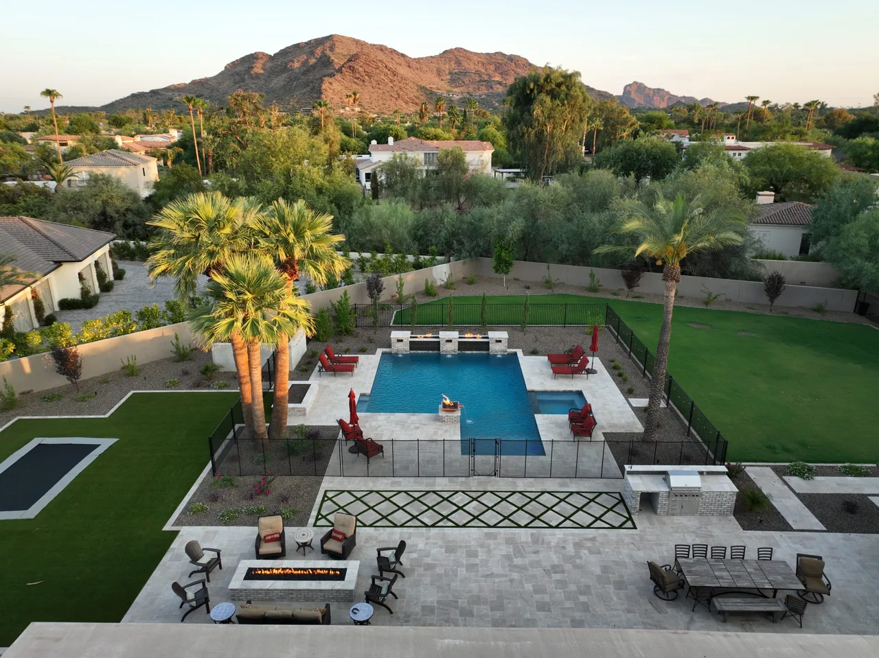 Aerial view of a rectangular pool with a fire pit, turf and palms below a mountain