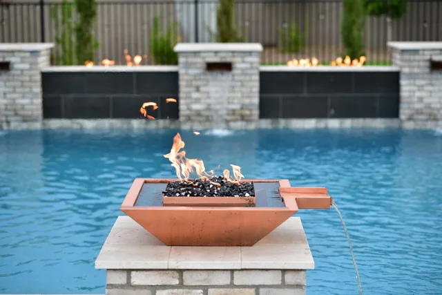 Custom fire features: Copper fire and water bowl on a stone column in a blue pool