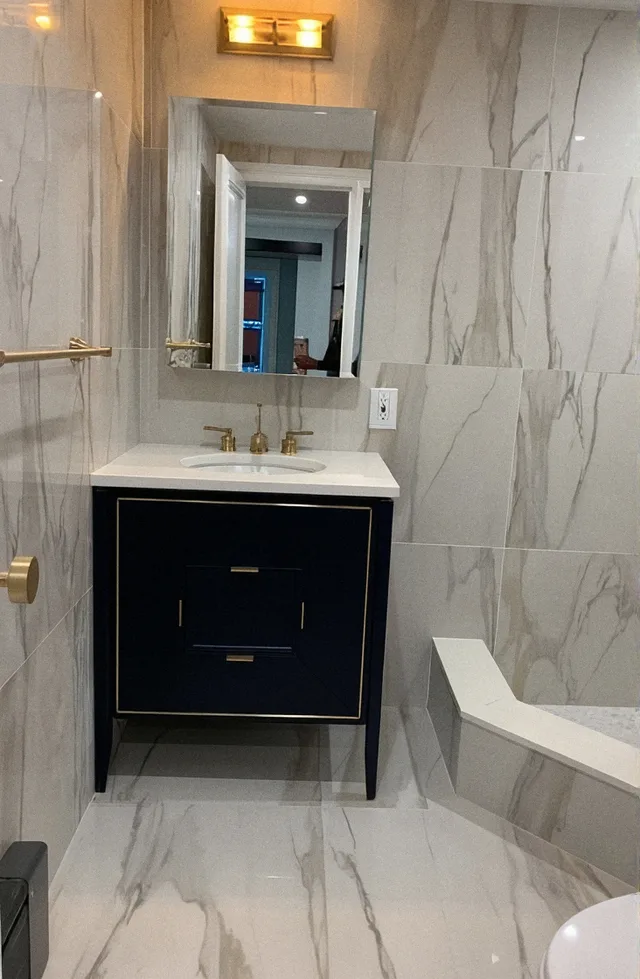 Bathroom Remodel 3: Bathroom after the remodel, marble tile with a navy vanity and brass fixtures